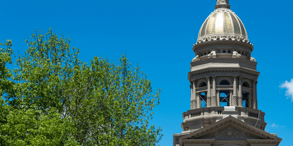 View of the Cheyenne Capitol building, showcasing its gold dome, neoclassical architecture, and surrounding landscaped grounds under a clear blue sky.